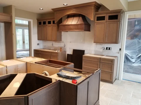 Traditional kitchen cabinetry installation in progress with decorative wood hood
