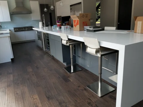Finished modern gray kitchen cabinetry with long white countertop and seating area