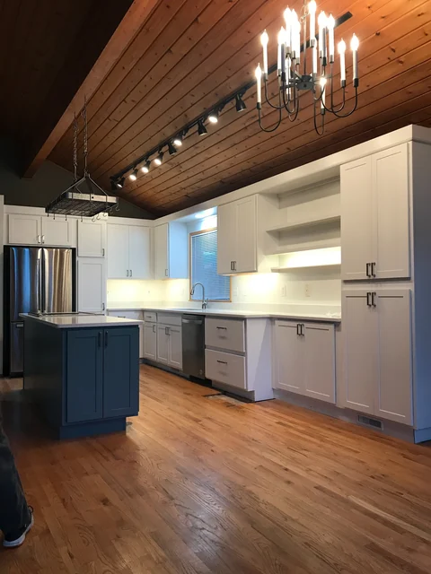 Finished white kitchen cabinetry under a vaulted wood ceiling with a contrasting island